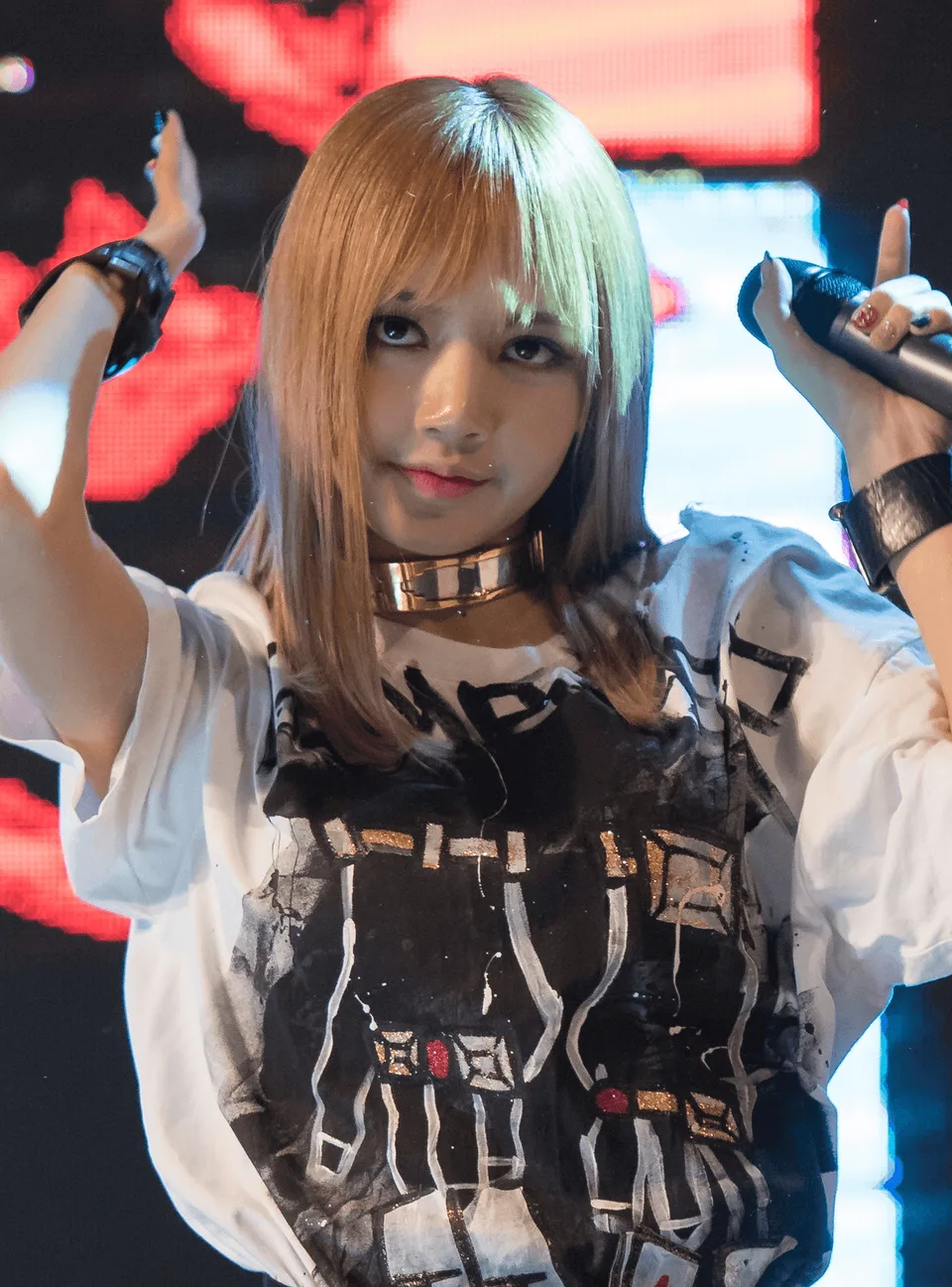 Blonde Lisa raises both arms onstage while holding a microphone · photographed in 2017