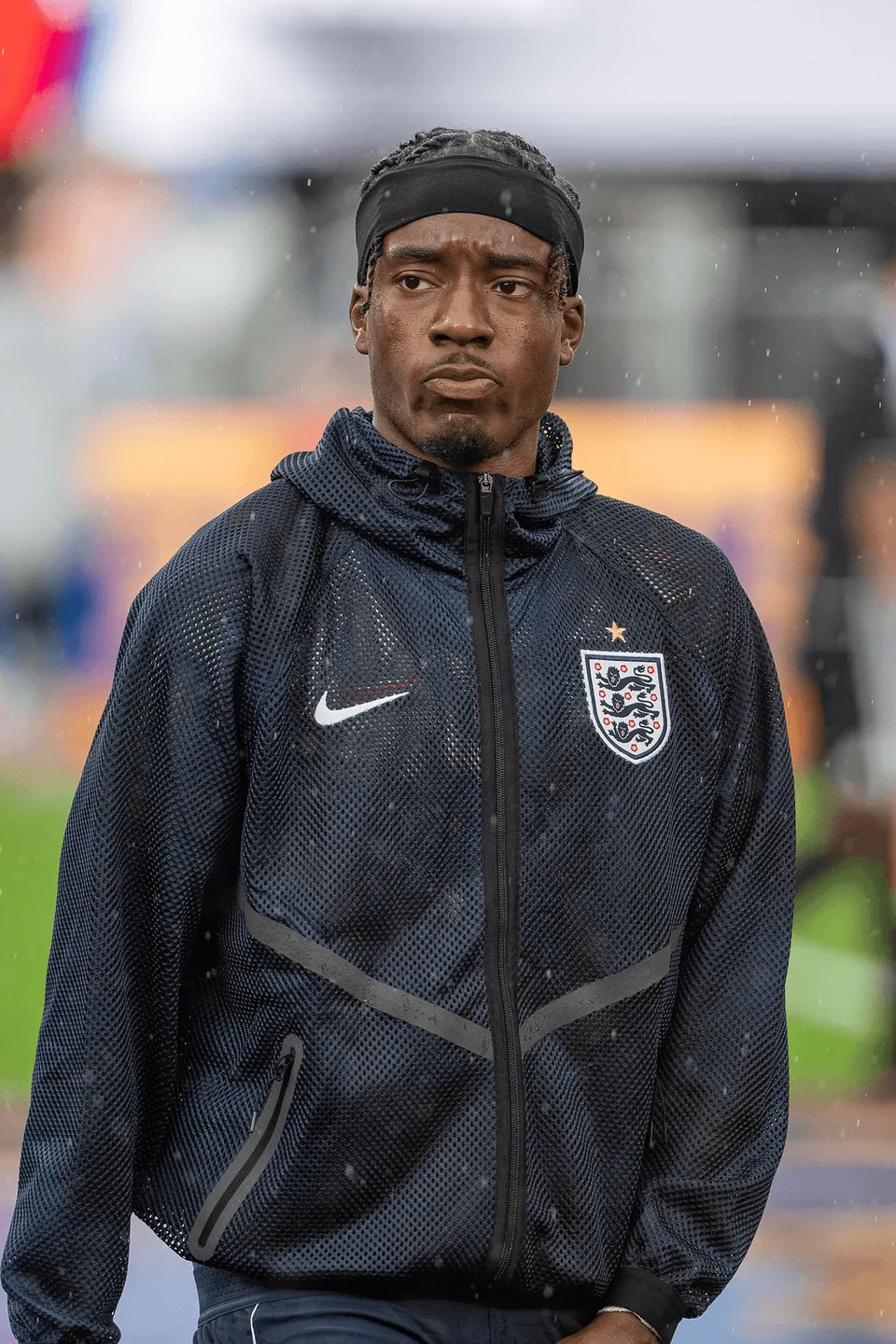 Noni Madueke standing in the rain wearing an England team jacket. · On-location photograph · Photographed in 2026