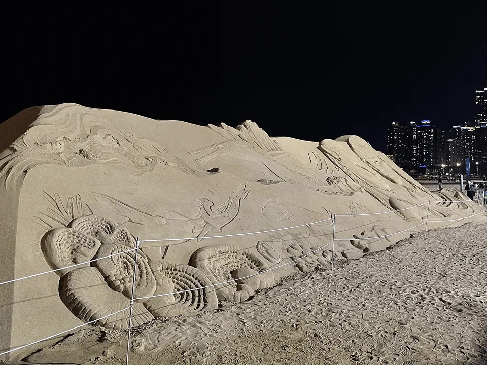 A large sand sculpture promoting “Avatar: The Way of Water” on a beach at night · Photographed in 2022